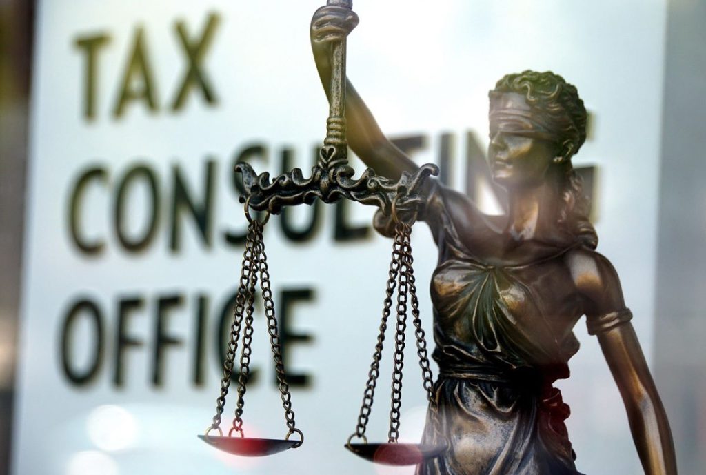 Statue of Lady Justice holding scales in front of a blurred tax consultation office sign